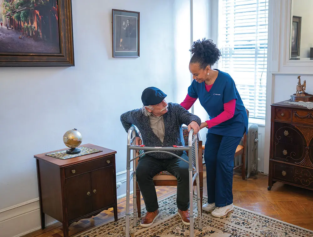 home health aide helps older man with walker to prevent falling
