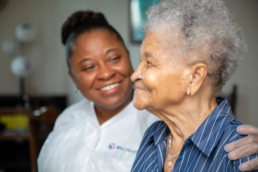 A caregiver with her arm around an older woman