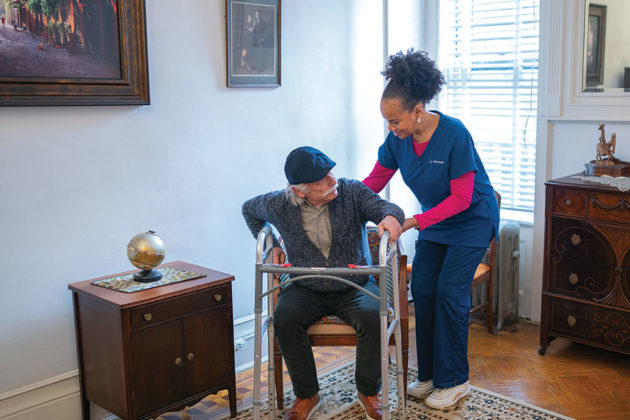 home health aide helps older man with walker to prevent falling