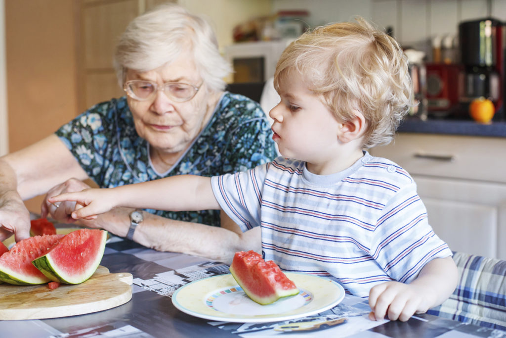 A grandmother and her grandchild eat watermelon together to stay hydrated.