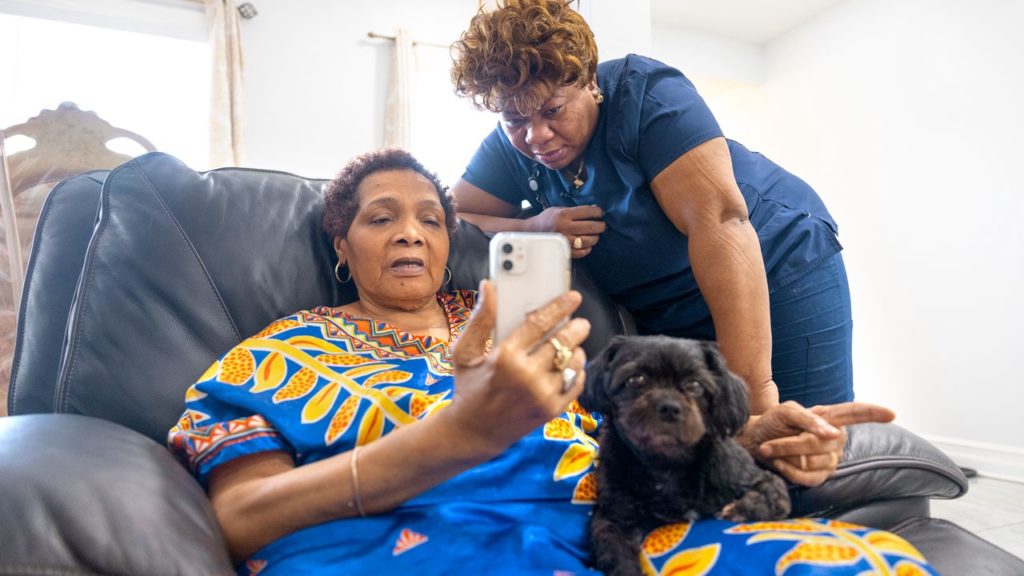 Picture of home health aide Marie Dorviline with her client, Yanick looking at Yanick's phone with a dog on her lap.