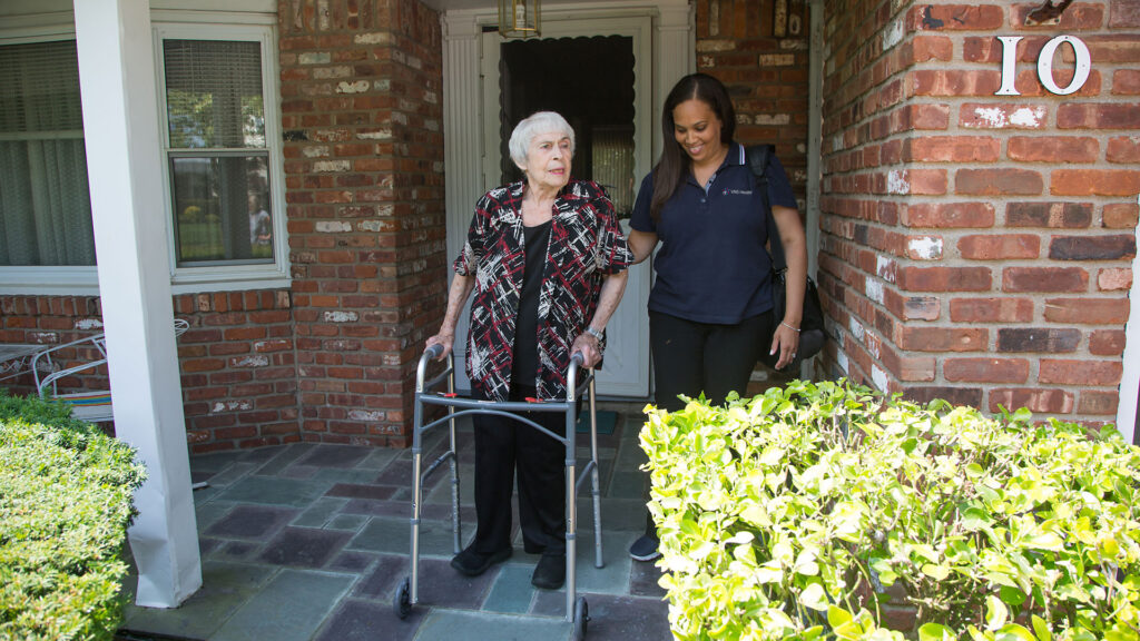 VNS Health team member helps senior woman with walker as they go outside.