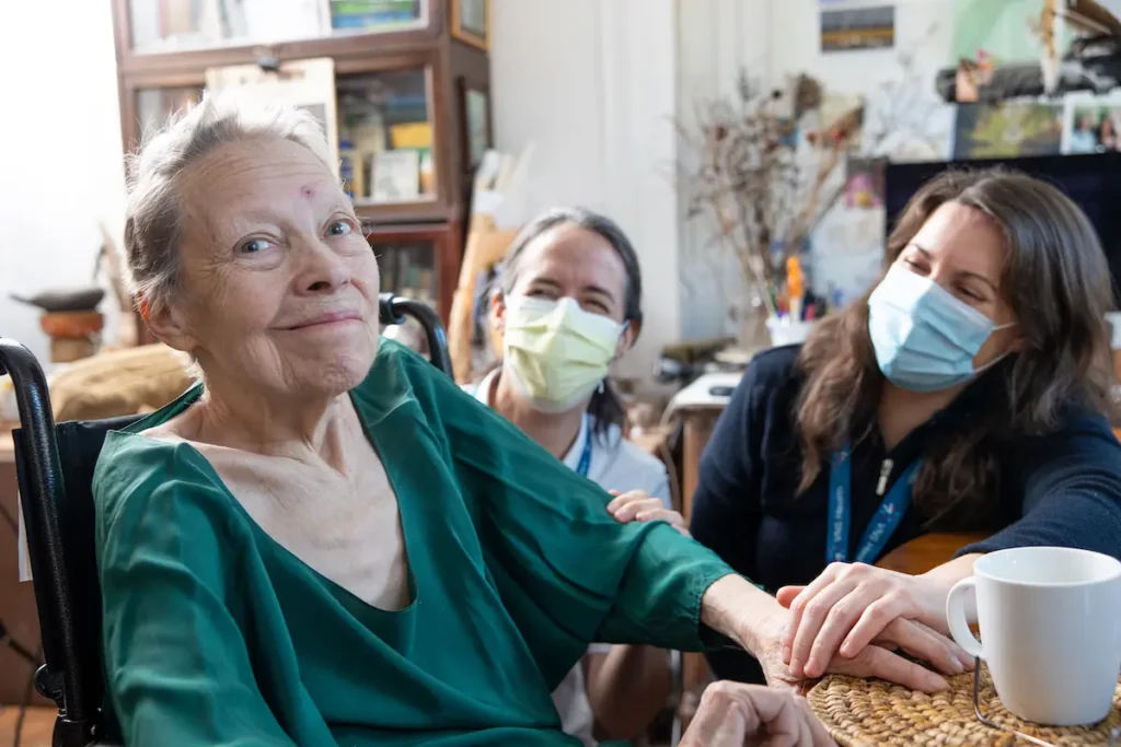Kathy sitting near a table with 2 VNS Health team members in masks with her.